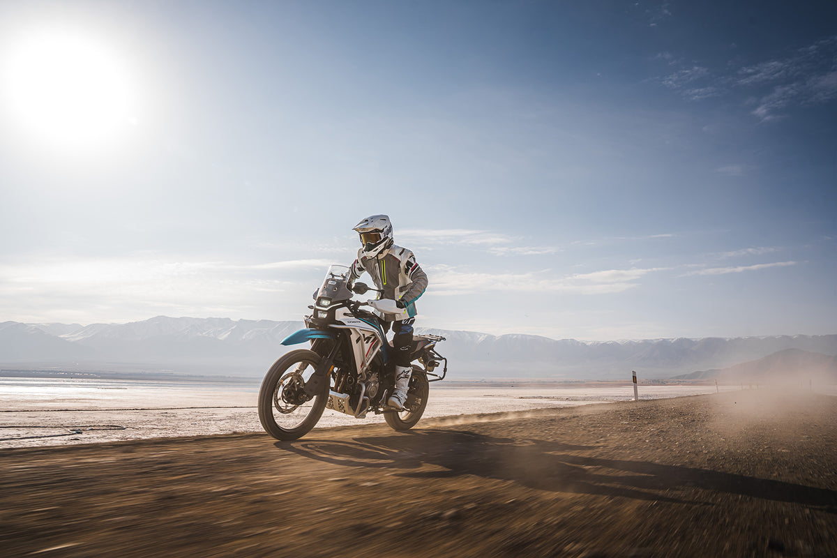 CFMOTO 450MT riding on a desert road with mountains in the background