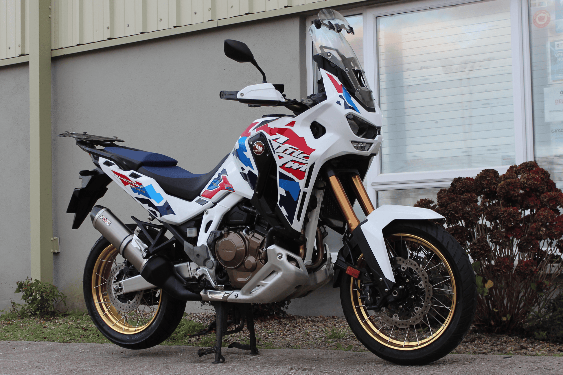 White blue and red adventure bike with gold wheels on centre stand